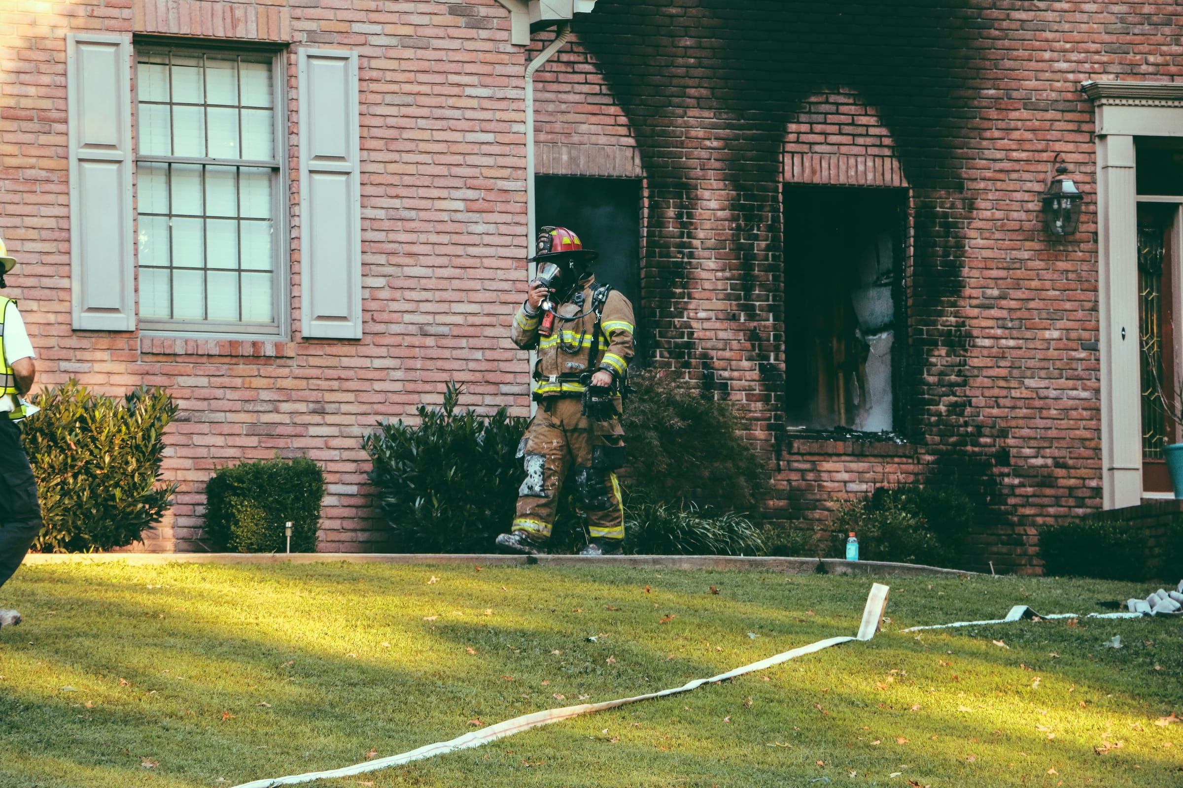 A firefighter outside a brick house with smoke damage around the door